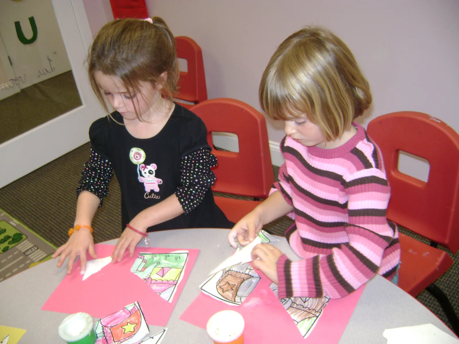 Two SELA students work side by side on a paper craft project at a classroom table.