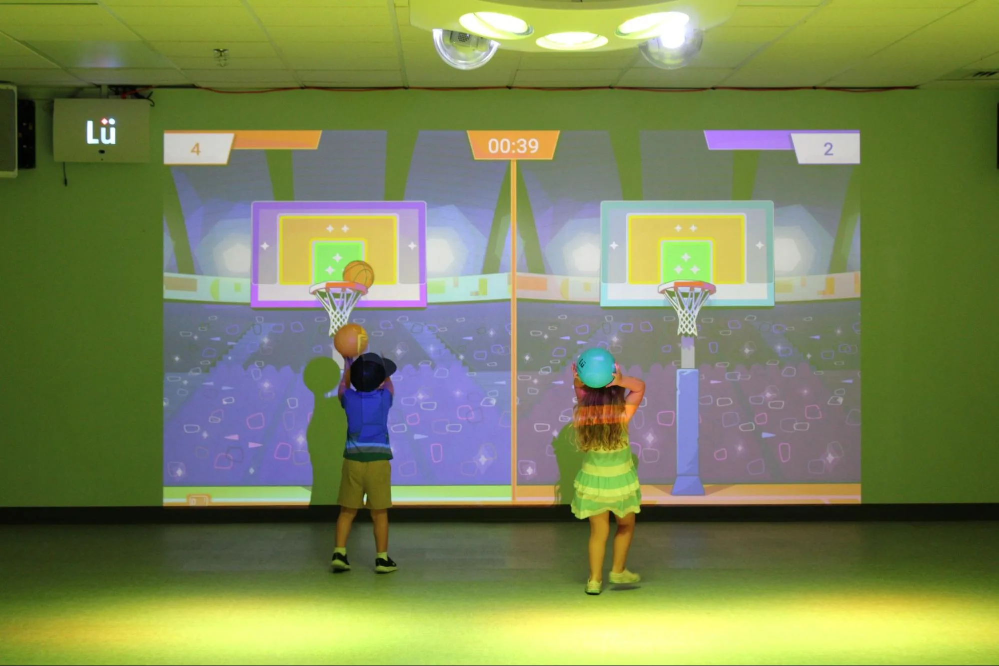 Two young SELA students throw balls at an interactive projected game on the LU interactive system wall.