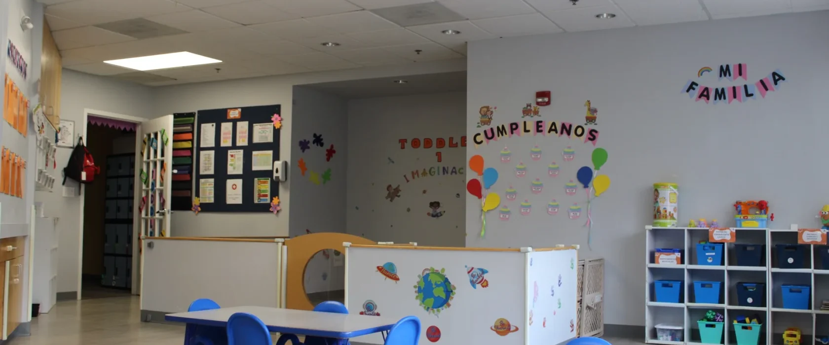 A bright Spanish-immersion Toddler classroom at SELA — Mi Familia wall décor, a world map, and warm, colorful learning spaces