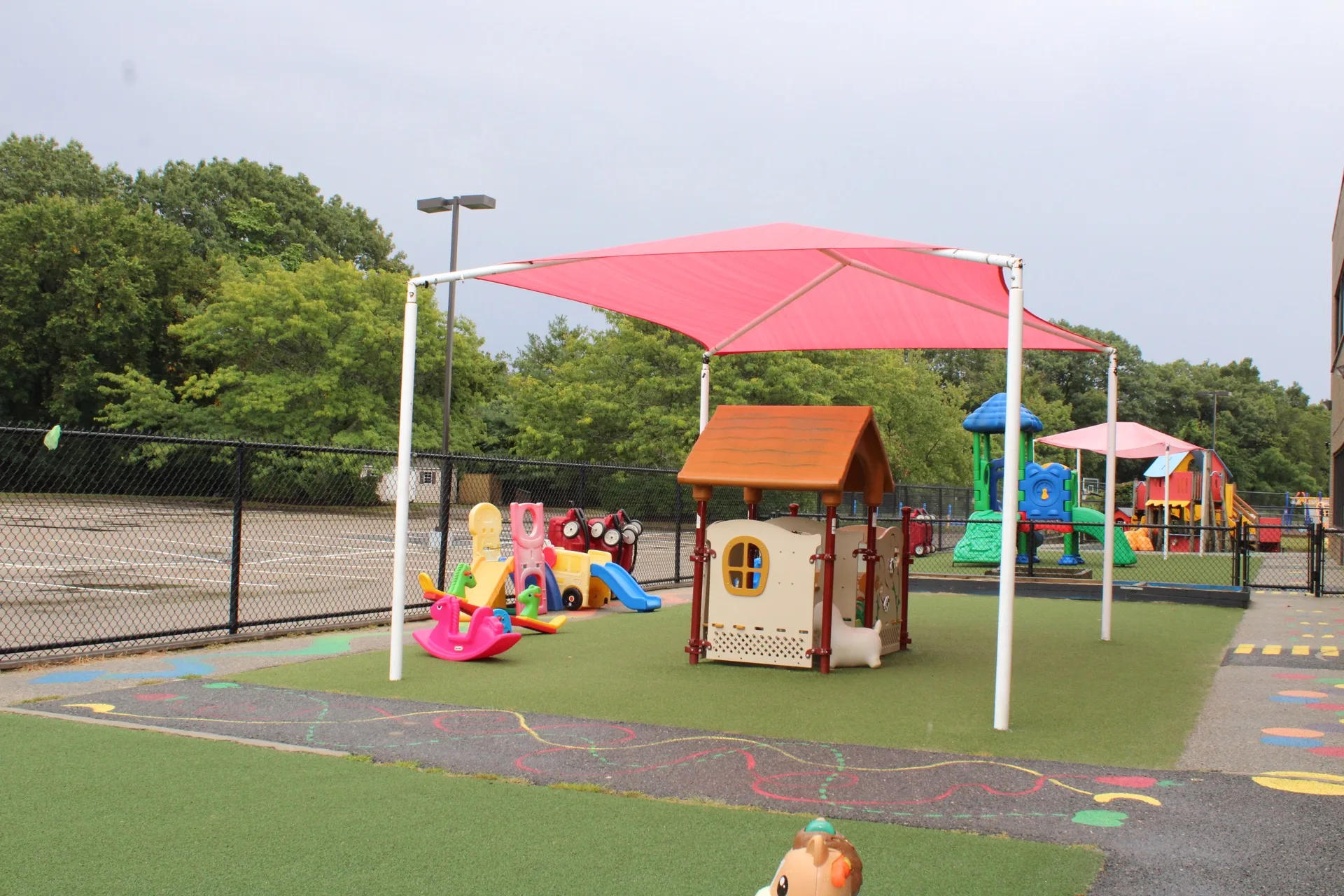 An outdoor playground at SELA's Hingham campus, shaded by a canopy, with a playhouse and climbing structures.