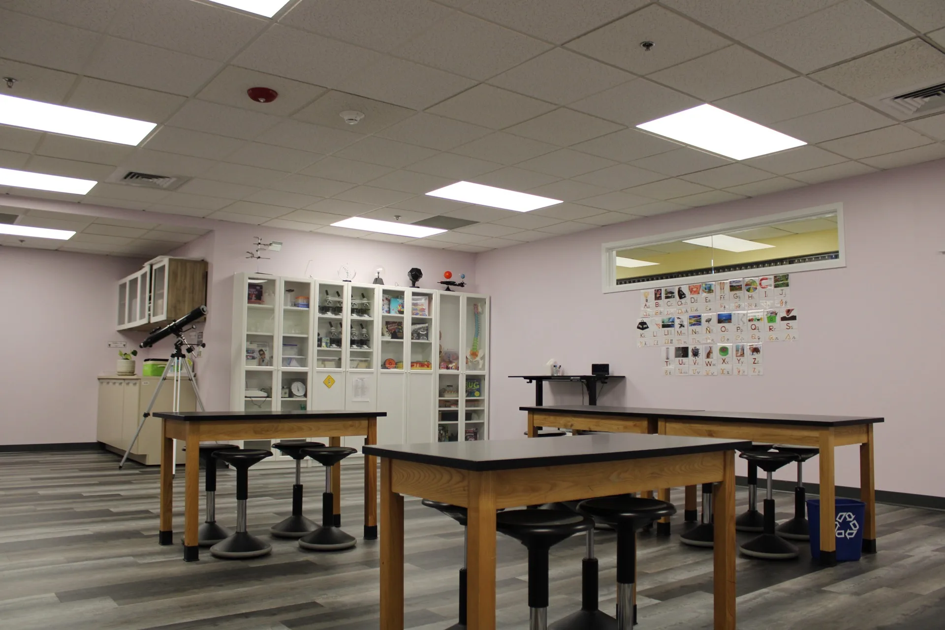 A science lab at SELA's Hingham campus, with black-topped lab tables, stools, a telescope, and equipment cabinets.