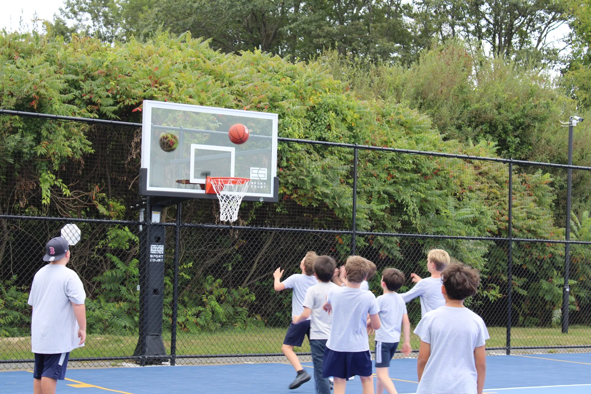 A cluster of SELA children jump and reach for a basketball at the hoop on the outdoor court.