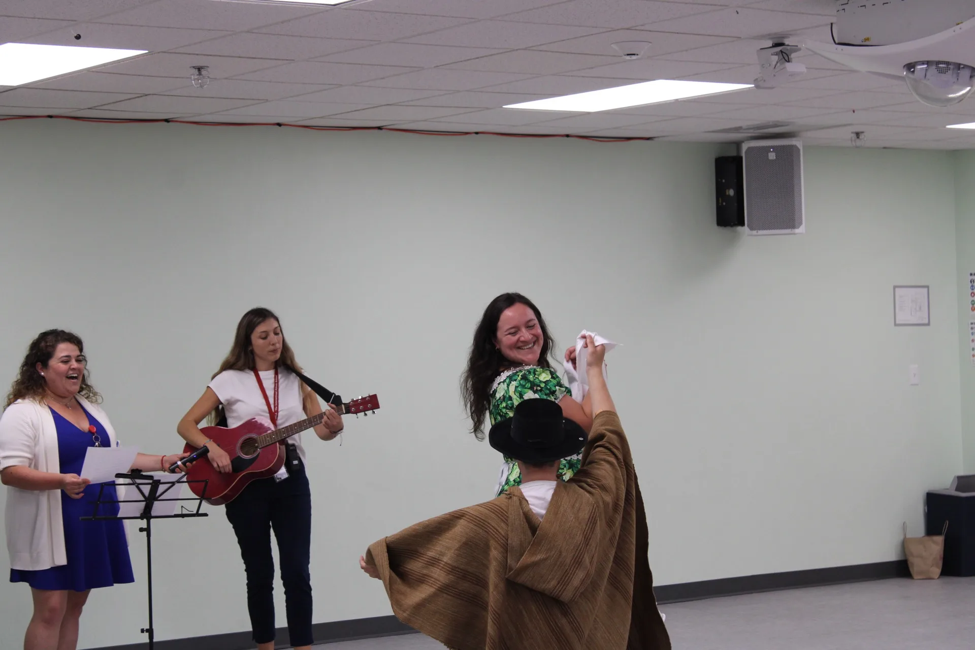 A SELA staff member twirls in a folk dance wearing a traditional poncho and hat as colleagues sing along.