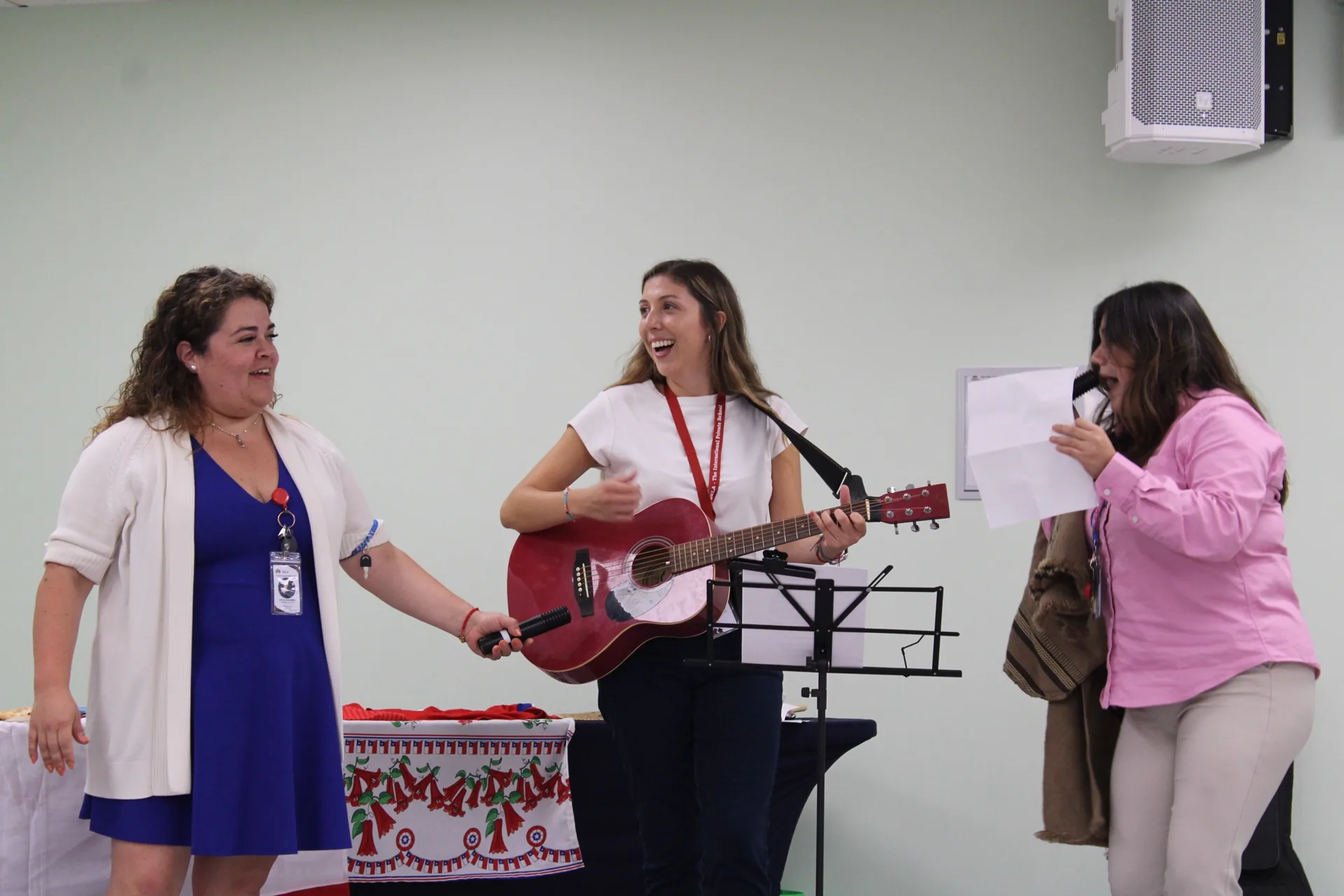 Three SELA teachers perform live music together, one playing guitar and singing, during a school celebration.